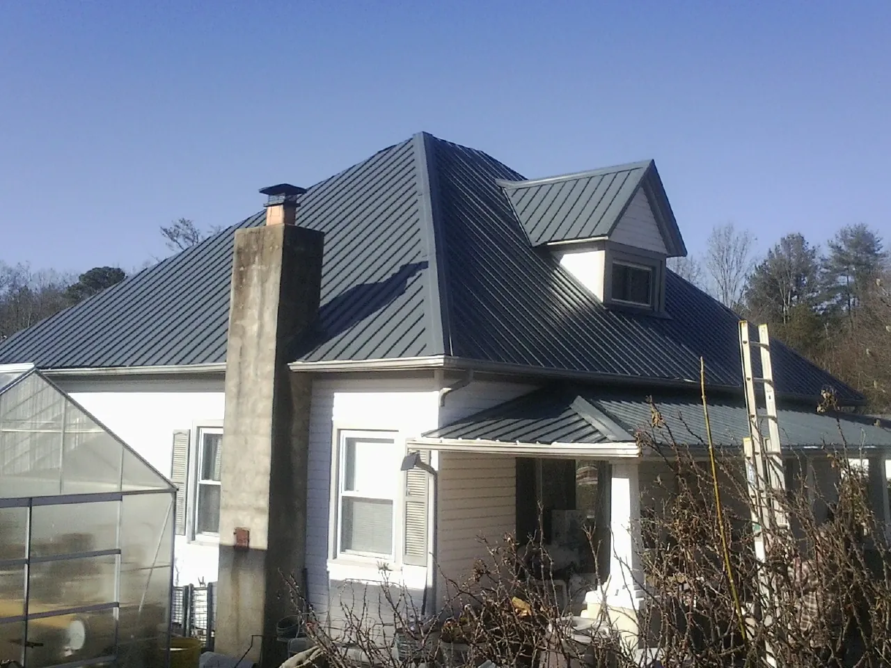 Dark blue standing seam metal roof on a white farmhouse with dormer — Slate & Tile Roof Repair by Roofing Brothers in Winona