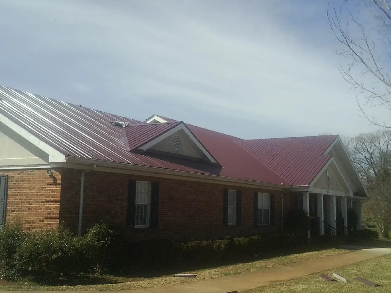 Red metal roof with gabled entries on a long brick building, from a Hail Damage Roof Repair job in Winona