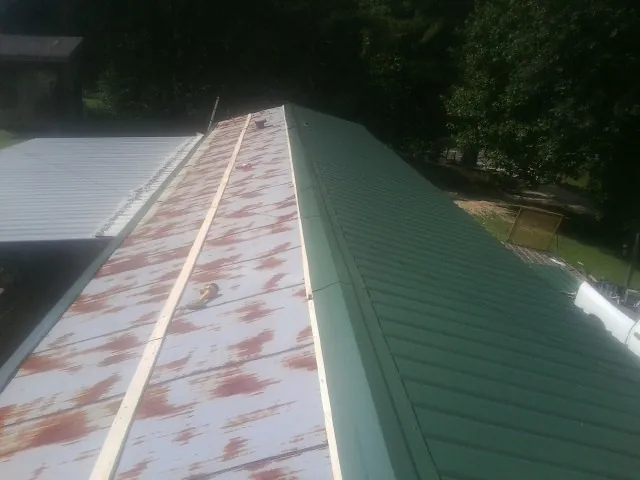 Old rusted panels beside newly installed green metal roofing — Wind Damage Roof Repair by Roofing Brothers in Winona