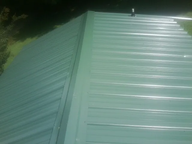 New green metal panels meeting at the ridge of a roof — Flat Roof Repair work by our crew in Winona