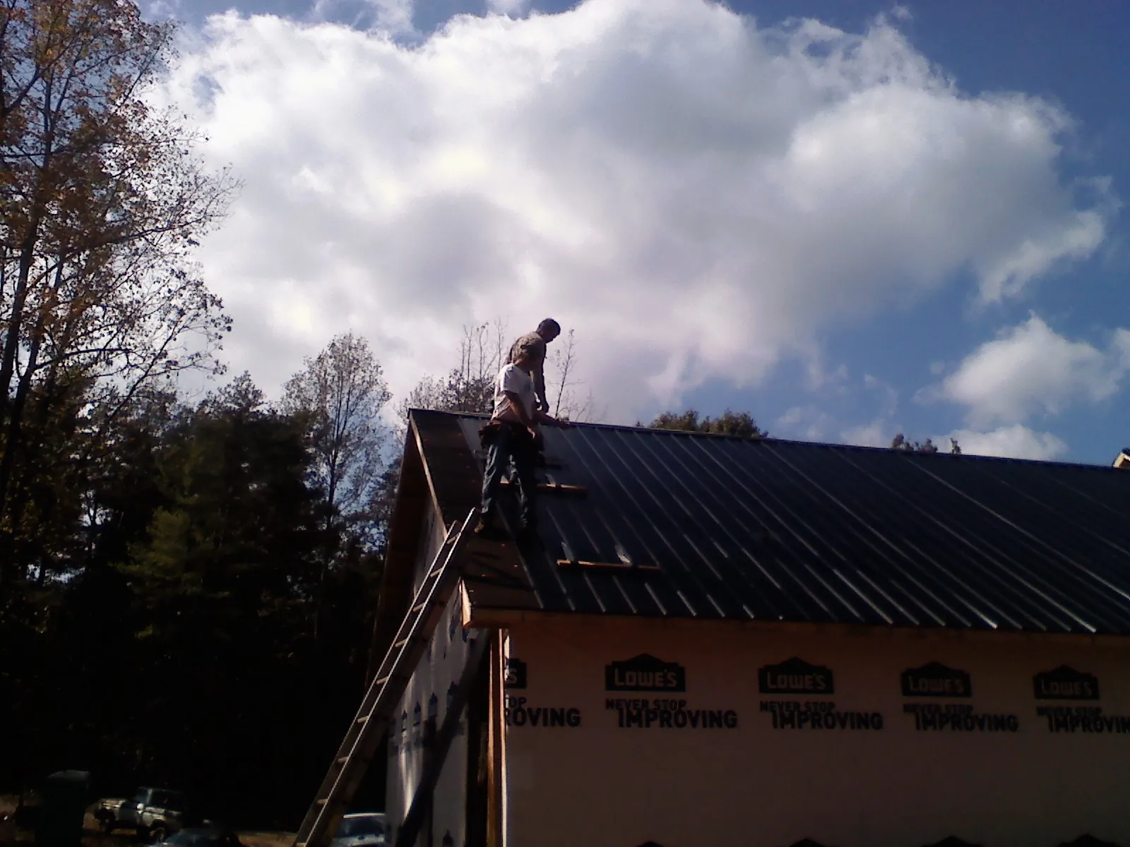 Roofer fastening dark metal panels high against a cloudy sky, from a Roof Inspection job in Winona