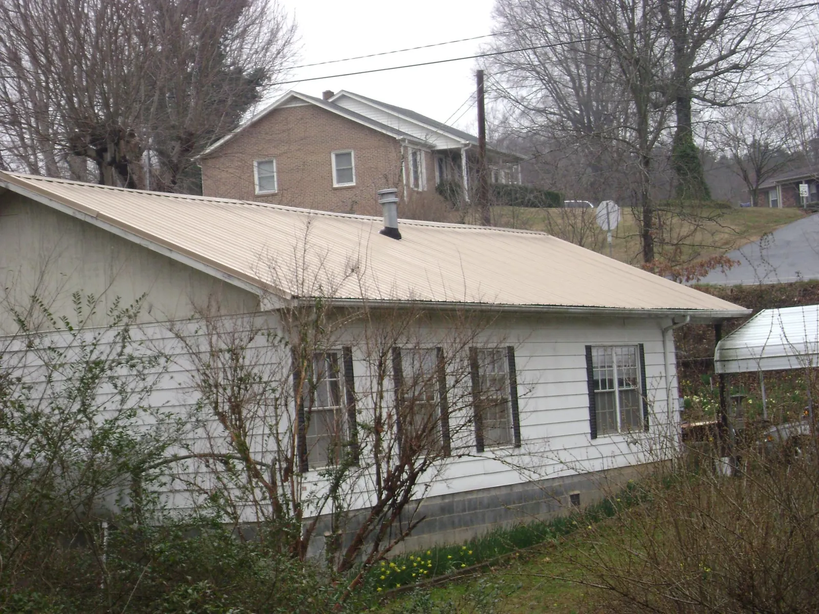 Tan metal roof on a white sided house set into a hillside — Commercial Roofing by Roofing Brothers in Winona